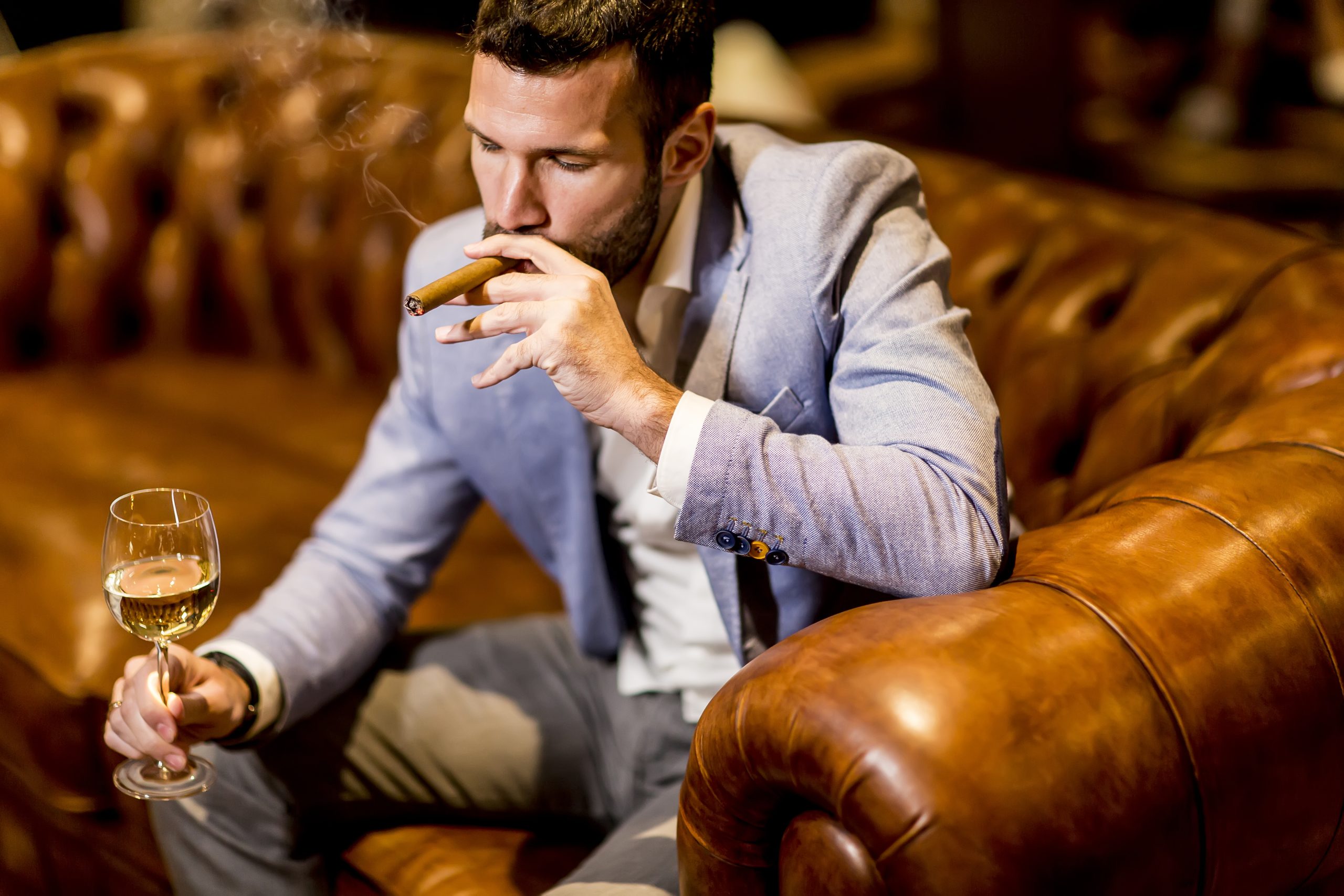 Young man tasting white wine and smoking cigar